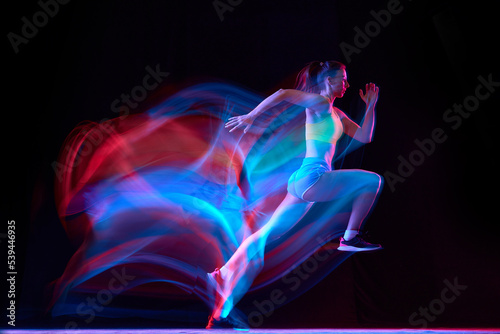 Professional female athlete, runner in motion over dark background in mixed neon light. Art, beauty, sport, cyberpunk concept