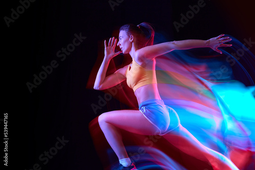 Fototapeta Naklejka Na Ścianę i Meble -  Speed. Professional female athlete, runner in motion over dark background in mixed neon light. Art, beauty, sport, cyberpunk concept