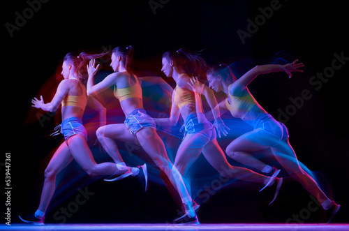 Development of movements. Professional female athlete, runner in motion over dark background in mixed neon light. Art, beauty, sport, cyberpunk concept