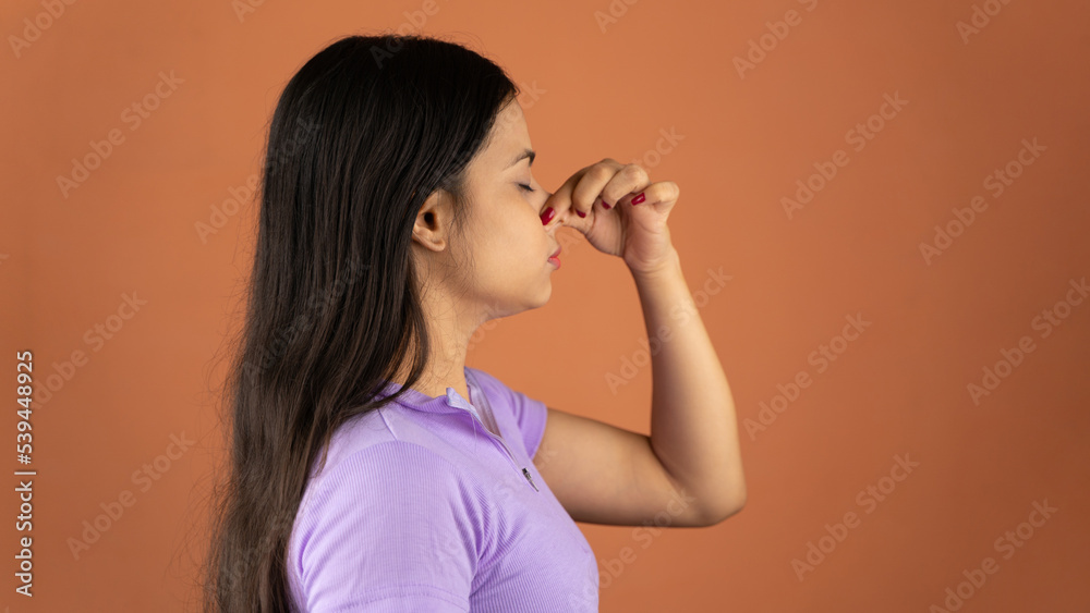 Portrait of young woman pinching nose with disgust on his face due to bad smell isolated over color background Portrait of young woman pinching nose with disgust on his face due to bad smell isolated over color background