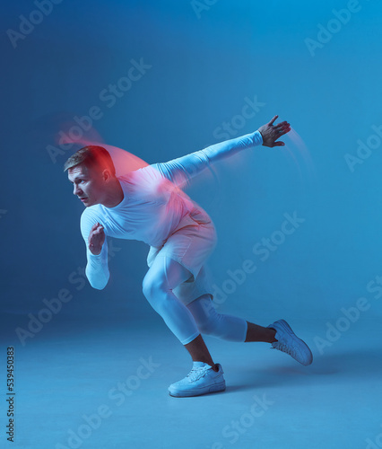 Sprinter start. Male strong muscular athlete starts running on blue background.