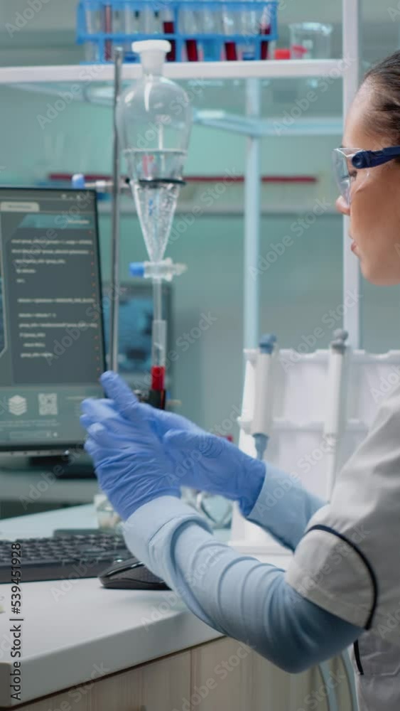 Vertical video: Innovation scientist studying petri dish with liquid bacteria while using modern computer with cell animation in laboratory. Woman with lab coat and glasses doing pharmaceutical Vertical video: Innovation scientist studying petri dish with liquid bacteria while using modern computer with cell animation in laboratory. Woman with lab coat and glasses doing pharmaceutical