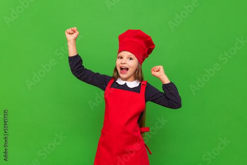 A teenage girl has put on a chef's uniform and is very happy that she will cook breakfast, a child in the form of a cook on an isolated green background.
