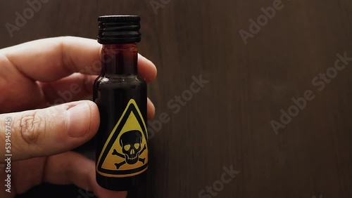 hand holding a small bottle of poison with a yellow toxic sign represented by a skull and two bones icon - dangerous concoction or brew for a poisoning to drink or inject