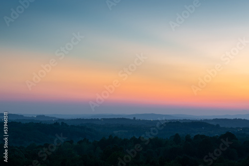 Hill layers separated with haze and vibrant glow in sky above horizon at twilight, hilly rural landscape with last light on clear sky © slobodan