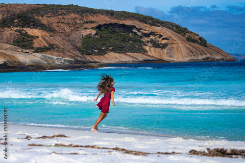A long-haired girl in a dress dances, runs and fools around on a paradise Australian beach; white sand and turquoise water in cape le grand national park