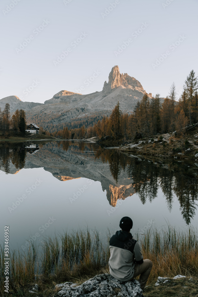 Ein Mann spaziert bei den letzten Sonnenstrahlen am Lake Fedare / Lago di Federa in den Belluner Dolomiten zum Sonnenuntergang. Es ist Herbst in den Dolomiten und der Berg spiegelt sich 1