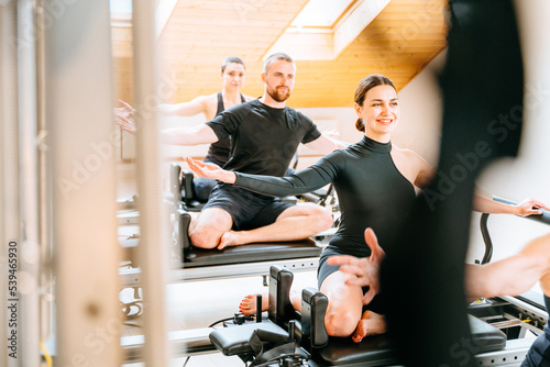 Rehabilitation, healthy lifestyle, small business concept. Sportive people making different exercise while workout with reformer bed at modern pilates studio.
