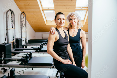 Portrait of two business parner different age pilates female instructor in black sportwear posing with sport equipment on background. photo