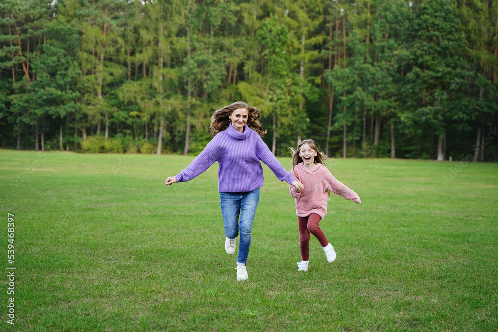 Happy mom and daughter run outdoors. Joyful girl and woman have fun together. Family vacation in nature