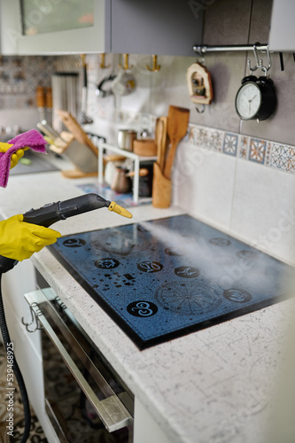 Cleaning a stylish electric stove with a steam generator. Steam cleans the surface from dirt. White kitchen. Cleaning in the apartment. photo