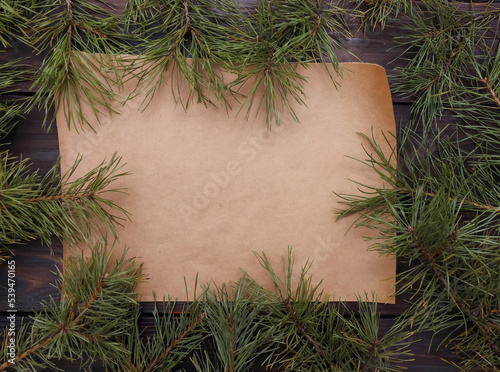 Frame of Christmas pine tree branches on dark rustic wooden table with copy space on blank retro craft paper piece. Xmas background  New Year  winter holiday  nature flat lay. Copy space  top view