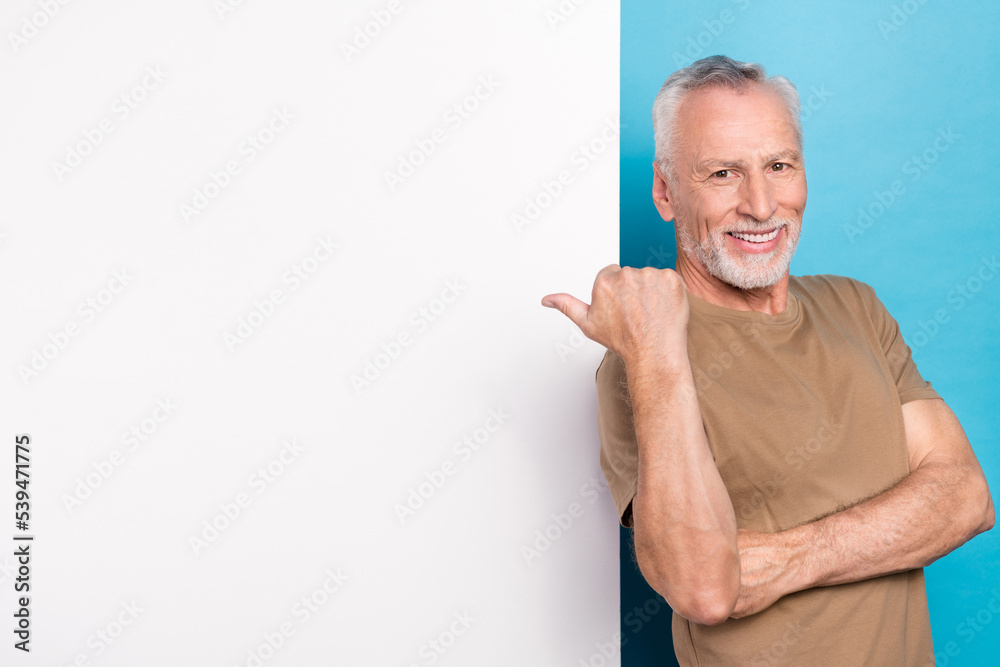 Portrait of positive cheerful retired man with gray hair beard beige t-shirt directing empty space isolated on blue color background Portrait of positive cheerful retired man with gray hair beard beige t-shirt directing empty space isolated on blue color background