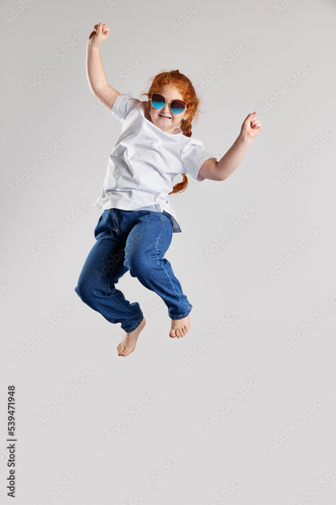 Delight. Happy little girl, kid in white t-shirt and jeans jumping high isolated over white background. Kids fashion, emotions, carefree childhood