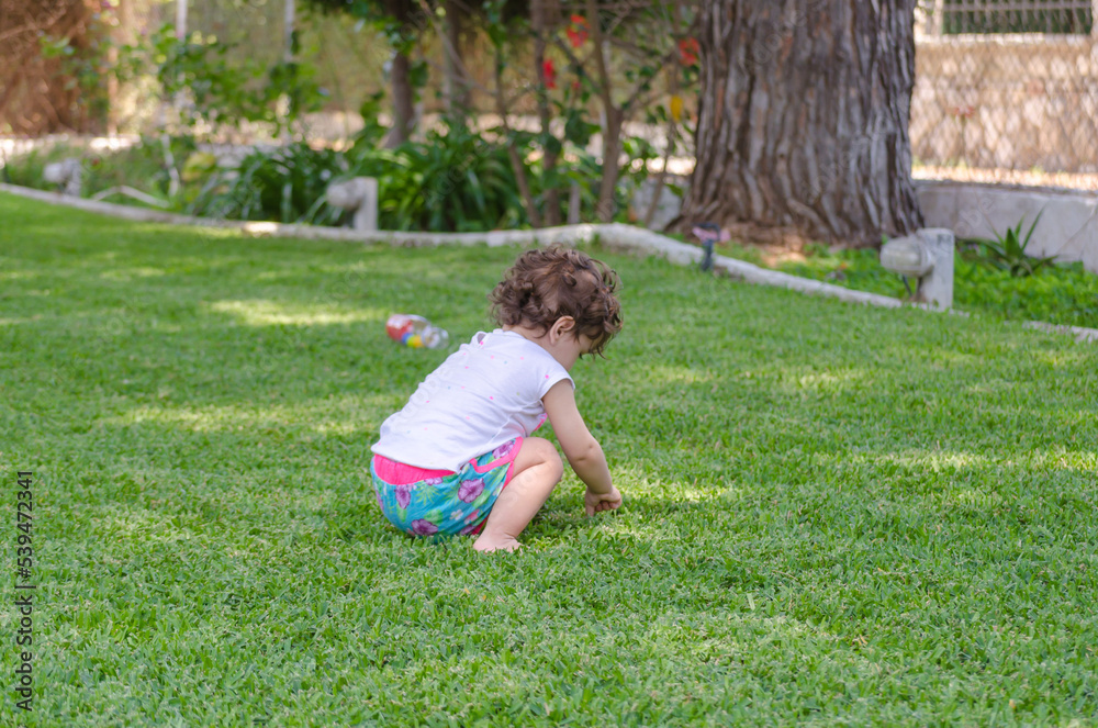 Curious Toddler Kid Explores the Green Grass in the Garden. Baby Girl Plays in a House Backyard on a Sunny Day in Greece Curious Toddler Kid Explores the Green Grass in the Garden. Baby Girl Plays in a House Backyard on a Sunny Day in Greece