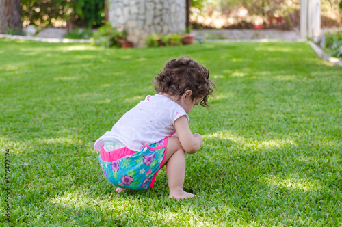Curious Toddler Girl Explores the Green Grass in the Garden. Kid Play in a House Backyard on a Sunny Day in Greece