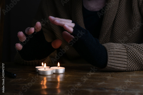 Obraz na płótnie Man in sweater and fingerless gloves warming up his hands with tealight candles during energetic crisis in Europe. w salonie