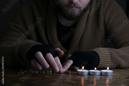 Obraz na płótnie European poor bearded man counting euro coins during energy crisis in Europe. A worried man in warm sweater and gloves counts money in candlelight. w salonie