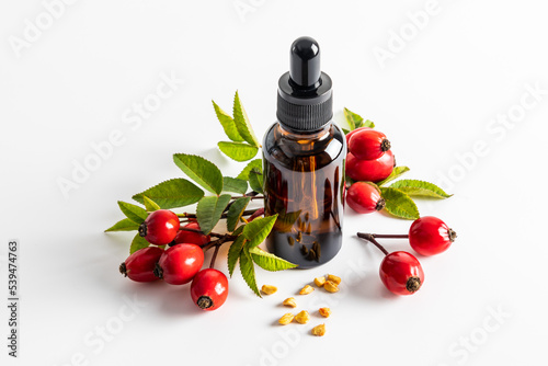 serum based on rosehip seed oil for facial skin care in a cosmetic bottle on a white background among ripe rosehip berries. moistening. nutrition. photo