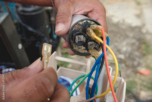 An AC technician removes a defective capacitor from a window type air conditioner control panel. photo