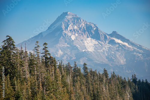 Mt Hood rises in the distance over Lost Lake in Oregon mid-afternoon.  The blue lake and green pine trees from the majestic mountain. 