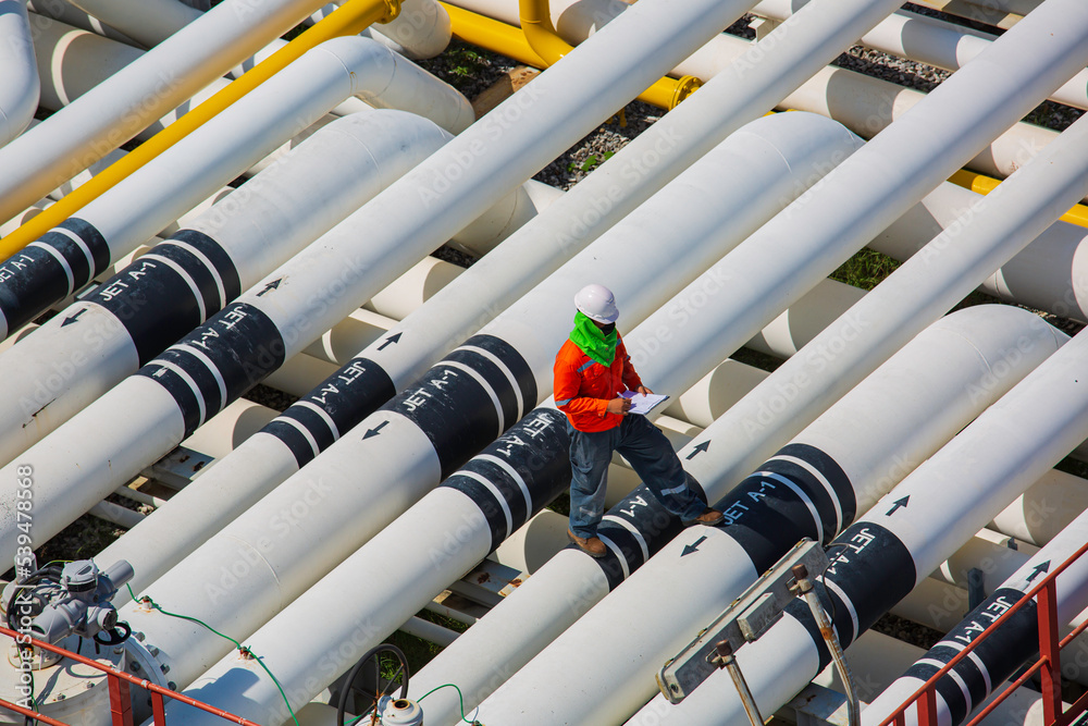 Top view male worker inspection at steel long pipes and pipe elbow valve in station oil factory during refinery valve of visual check record pipeline oil Top view male worker inspection at steel long pipes and pipe elbow valve in station oil factory during refinery valve of visual check record pipeline oil