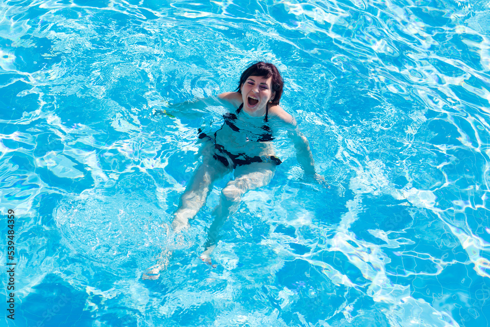 Young brunette woman swims in the blue water pool.