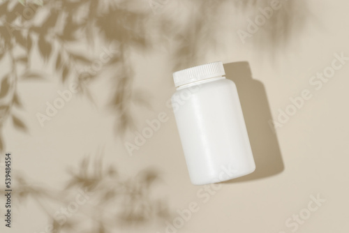 Vitamin medical bottle on beige background with leaves shadows, bio supplement, natural vitamins, minimal concept