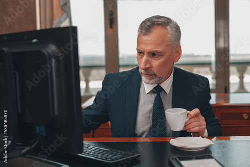 Male hotelier works at a computer and drink coffee while sitting in his office in a hotel photo