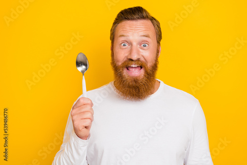 Photo portrait of handsome young guy hold spoon ready eat healthy food dressed trendy white pullover isolated on yellow color background