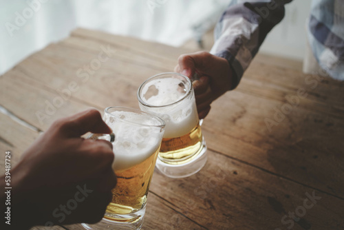 Two friends toasting with glasses of light beer on the wooden background. 