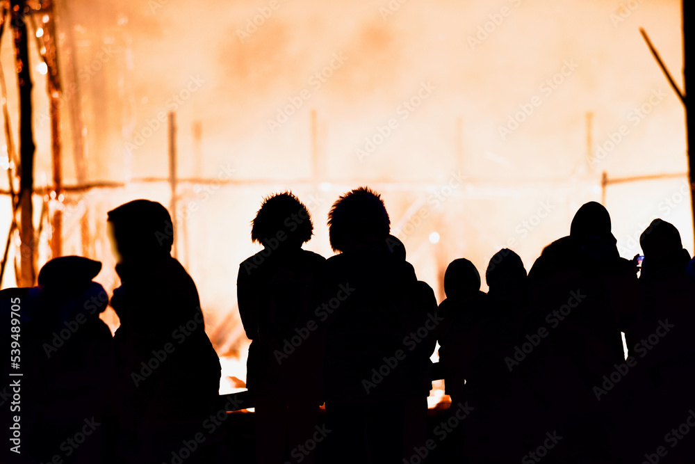 Dark silhouettes of people against the backdrop of a giant raging fire at night. The dark figures of a people against the backdrop of a burning building at night. People in front of the raging fire.