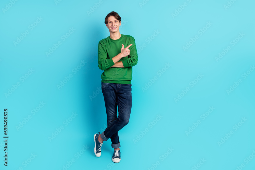 Full length photo of positive guy with folded arms point empty space shopping sale isolated blue color background Full length photo of positive guy with folded arms point empty space shopping sale isolated blue color background