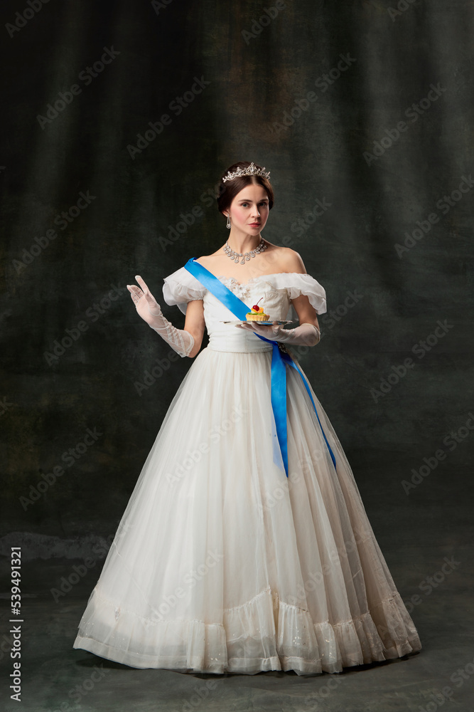 Fototapeta premium Young queen. Portrait of adorable girl in image of medieval royal person in renaissance style dress isolated on dark background. Comparison of eras, beauty, history, art