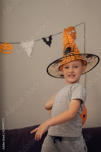 Boy with funny face in orange hat holding artificial pumpkin, halloween concept. High quality photo
