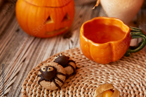 Aesthetics autumn decorations with Halloween spider cookies and cup of tea in shape of pumpkin. Jack o lantern