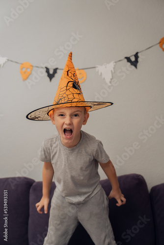 Boy in orange halloween hat with spider making funny and scary faces, halloween concept. High quality photo
