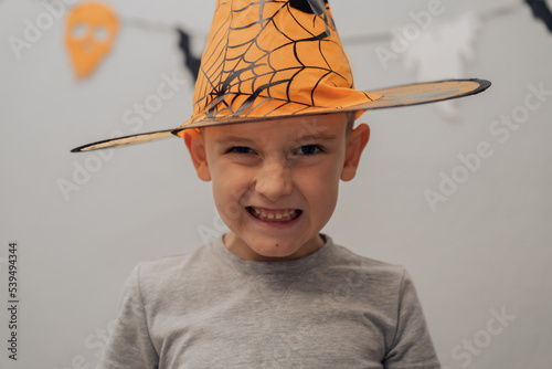 Boy in orange halloween hat with spider making funny and scary faces, halloween concept. High quality photo