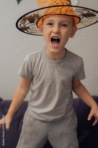 Boy in orange halloween hat with spider making funny and scary faces, halloween concept. High quality photo