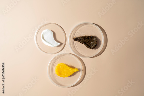 Three cosmetic smudges of body scrub and cream lying on plates on a beige background