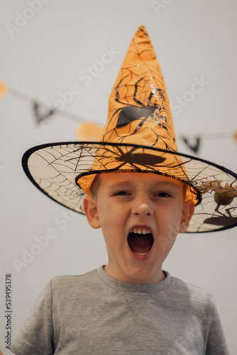 Boy in orange halloween hat with spider making funny and scary faces, halloween concept. High quality photo
