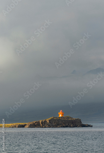 The bright-orange Aeoarstein Lighthouse in Djupivogur, east Iceland, sits atop harsh volcanic rock photo