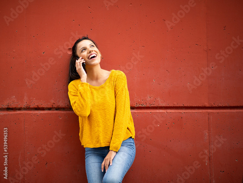 laughing latin woman with cellphone by red wall © mimagephotos
