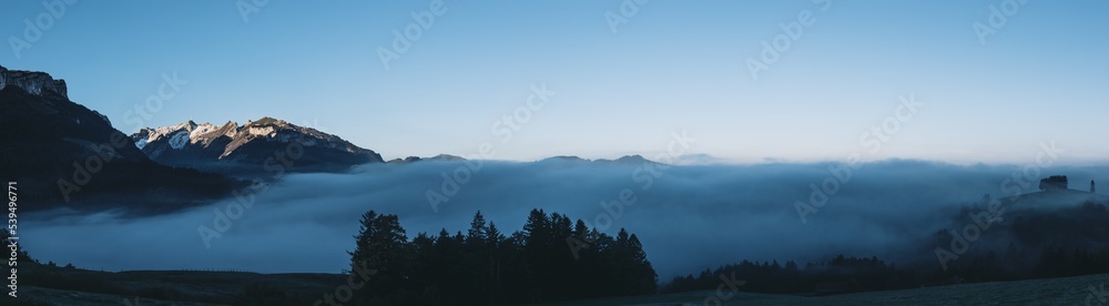 Panorama of the alpstein region. Morning fog and low clouds in the valley with the Säntis mountain in the first sunlight of the day. 
