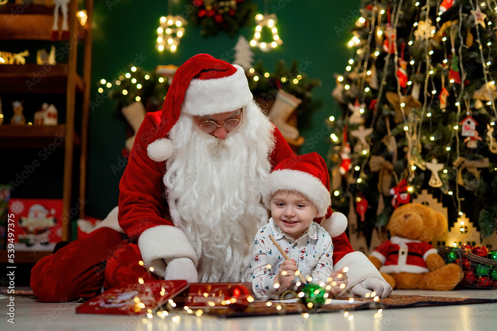 Little boy drawing with Santa Clause while lying on the floor near Christmas tree. New Year concept Little boy drawing with Santa Clause while lying on the floor near Christmas tree. New Year concept