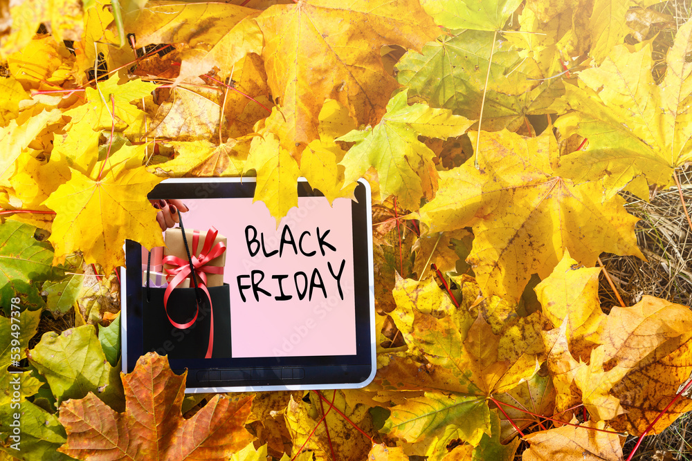 Black Friday sale concept. Tablet pad with sign Black Friday on screen, shopping bag, gift box over black background