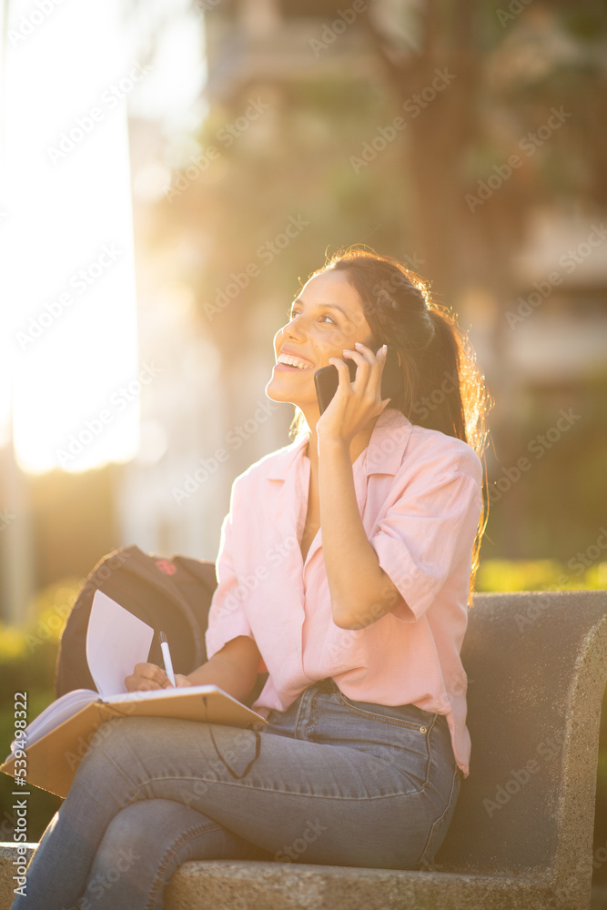 happy woman sitting outdoors with book and phone