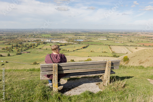 woman sitting alone on a bench overlooking a dramatic english landscape