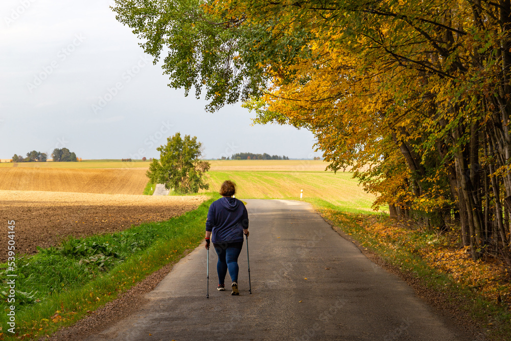 Fototapeta premium Plus size woman walking on the road. Nordic walking as healthy lifestyle and weight loss concept.