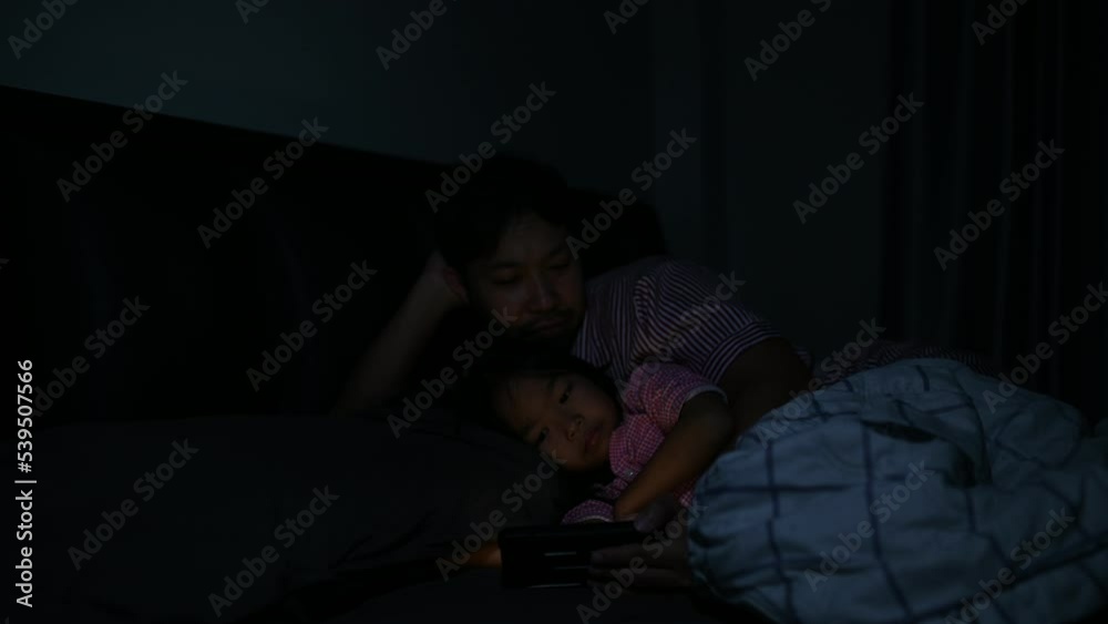 Dad and daughter sleep on the bed in bedroom,Watch cartoon with phone,Father day concept,Single dad,listen tale before sleep Dad and daughter sleep on the bed in bedroom,Watch cartoon with phone,Father day concept,Single dad,listen tale before sleep